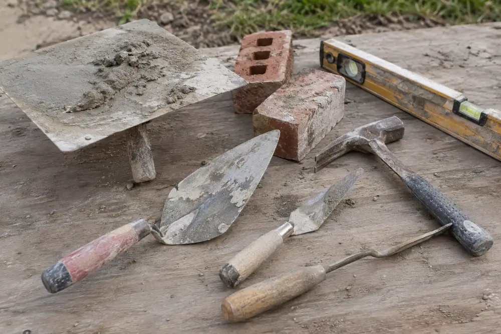 Mason's trowels, brick hammer, level and bricks on a wooden work surface